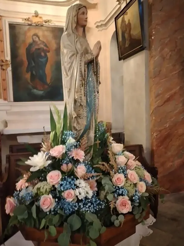 Composition de fleurs bleues et roses au pied d'une statue de la Vierge, dans une église