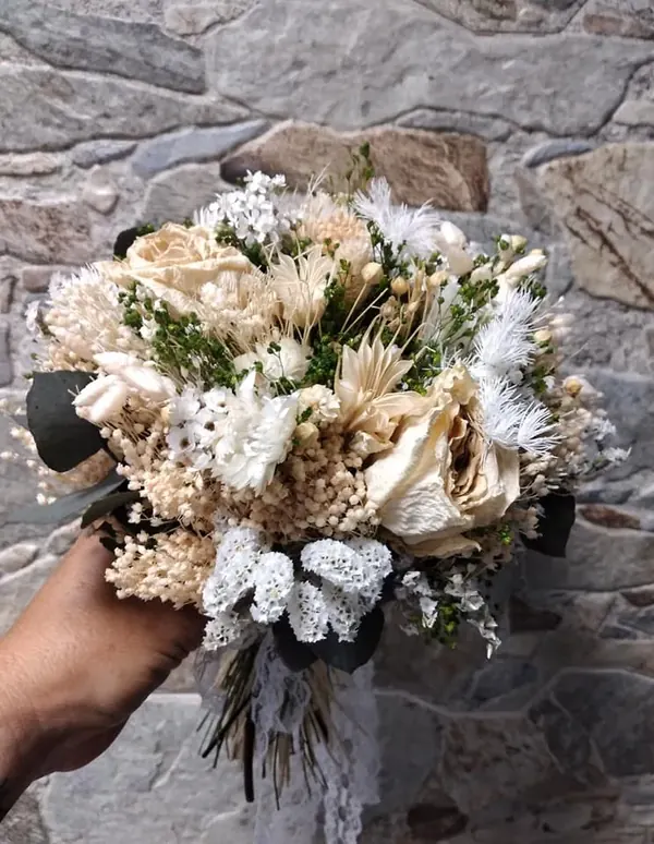 Bouquet de mariée blanc et crème, tenu à la main devant un mur de pierre